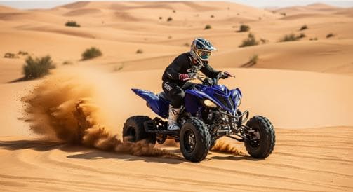 Rider maneuvering a Yamaha Raptor quad bike through the golden dunes of the Dubai desert under a clear blue sky - Yamaha Raptor Quad Biking Tours in Dubai